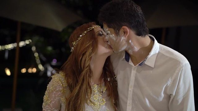 Girl smears a piece of wedding cake on the face of the groom. The celebration of the wedding at night.