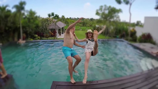 Young lovely couple photographed and fall into swimming pool at tropical vacation villa. Luxury resort or hotel.