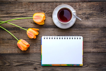 Romantic picture with tulips, tea, notebook on wooden background