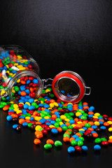 Scattered colorful coated candy from a glass jar. Black background with text space.