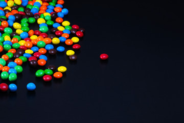 Scattered colorful coated candy spilled on a black background with text space. 