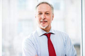 Bright portrait of a senior business man against a bright office background