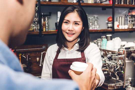 Woman barista behind the counter bar and giving coffee cup to customer at cafe