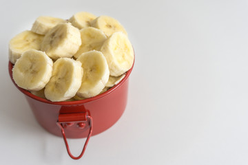 Red bowl with banana slices on white background