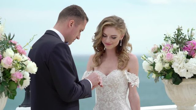 The bride and groom at the wedding ceremony. A young couple in love stands at the arch. Wedding by the sea. Exchanging rings.