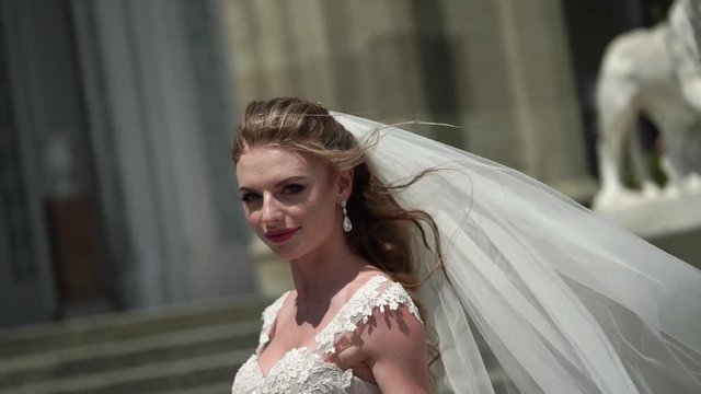 Young bride posing in a city. Waving veil at windy summer day. Slowmotion