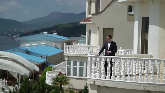 Man in classic black suit staying at the balcony near sea. Businessman or groom at wedding day