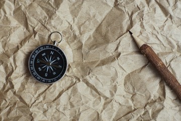 Compass, burnt brown paper and wooden pencil on crumples paper background, vintage tone, journey...