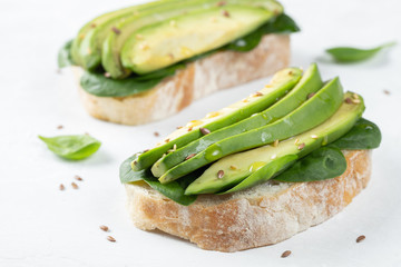 Two ciabatta toast with sliced avocado olive oil, spinach and flax and sesame seeds. Healthy vegetarian Breakfast on white background