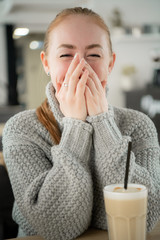 Young smiling woman sitting in cafe at table smiling with hands on her mouth. Hipster ginger, yawns, covering his mouth with hand.