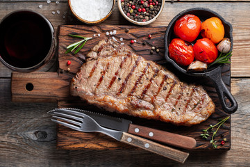 Steak Striploin, grilled with pepper, garlic, salt and thyme served on a wooden board. The finished dish for dinner with a glass of red wine on a old wooden rustic table. Top view
