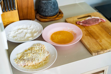Cooking pork homemade cutlet in kitchen, pork chop on chopping board , and ingredient powder and egg on plate, preparing for fired pork.