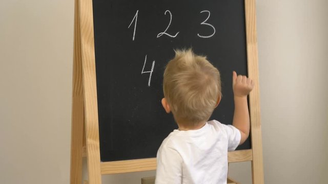 Cute little boy (toddler, two years old) is showing numbers on the chalkboard. Early childhood education to children concept.  Kindergarten, pre-primary, nursery school.