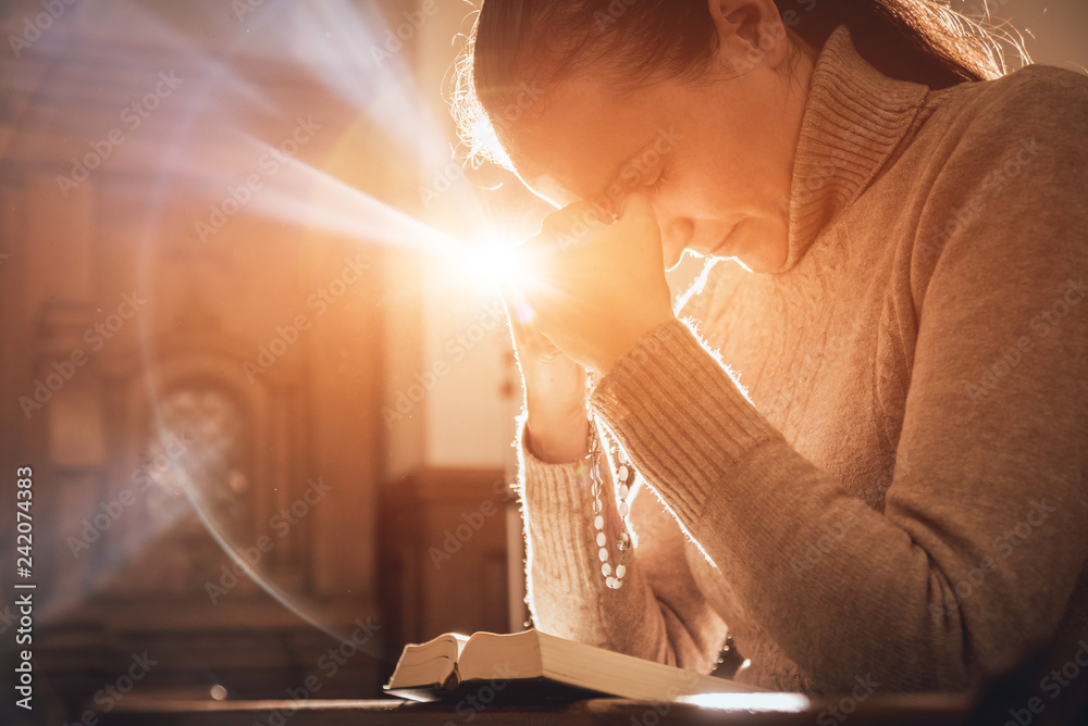 Wall mural christian woman praying in church. hands crossed and holy bible on wooden desk.