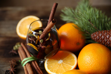 mulled wine in a glass with two sticks of cinnamon and spices, on oak wooden background, with a fir-tree branch close-up