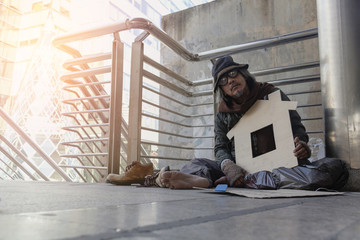 Homeless man is sitting down on walkway in town. He is hugging paper home. He is  hoping to have the better life. poverty, despair, Photo Sympathetic and hope concept.