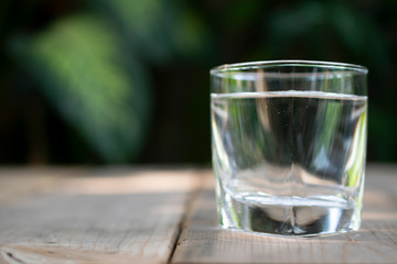 Drinking water in the glass on on the wooden table with green tropical tree at the background.