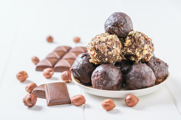 Homemade sweets made from nuts, dried fruits, chocolate and honey on a plate on a white table and a chocolate bar.