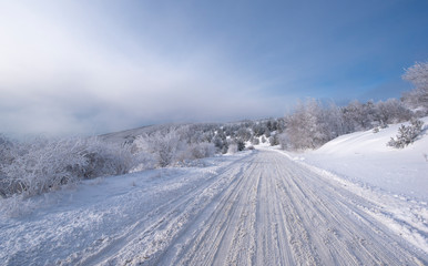 Fototapeta na wymiar Mountain winter landscape, an icy road leading towards The Buzludzha Monument in Bulgaria. View of empty road with snow covered through a forested Mountain
