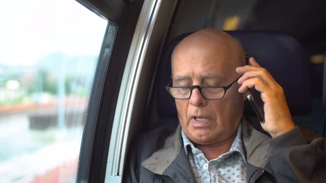Elderly man talking on mobile phone inside train