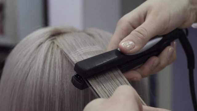 Woman Hairdresser Makes Patterns On Strands Of Hair Using An Ironing For A Beautiful Blonde Girl. Concept Of Preparation For The Holiday And Graduation