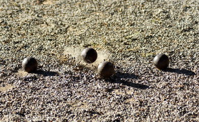 Throwing one petanque ball against another ball and impacting many other balls, until the small pebbles bounce along the impact.