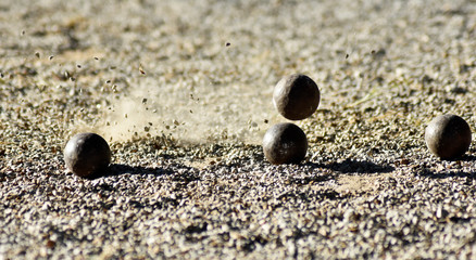 Throwing one petanque ball against another ball and impacting many other balls, until the small pebbles bounce along the impact.