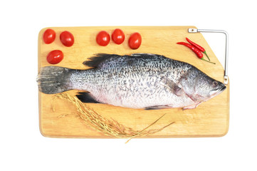 Fresh raw Asian Sea Bass fish  on wooden cutting board with chilli, tomato and raw rice on white background, top view. Seafood asian cooking ingredients.