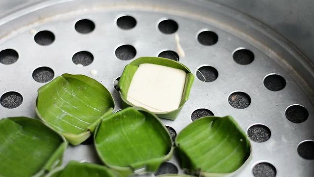 woman put dessert ingredient into small banana leaf bowl for steaming