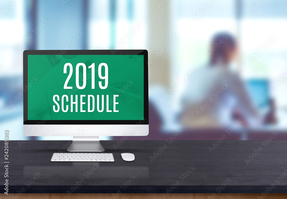 Poster 2019 schedule on desktop computer on black board wooden table top with blur people working at office desk bokeh background.