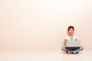 Asian little girl using a laptop , looking at camera and smiling against pink background.