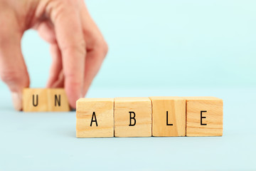 man hand spelling the text unable with wooden cubes, taking out the word un so it written able....