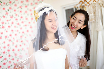 Beautiful bride getting dressed by her best friend in her wedding day and choosing a wedding dress in the shop and the shop assistant is helping her