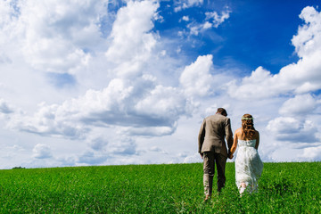couple walking in tall grass field with clouds and a bright blue sky on a farm