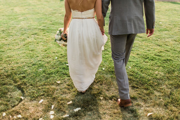 bride and groom holding hands walking in grass field