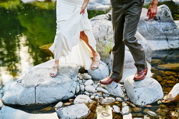 bride and groom standing on rocks near river at sunset