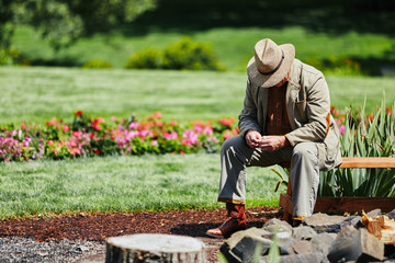 Naklejka na ściany i meble senior man sitting on bench on sunny day wearing a hat looking down