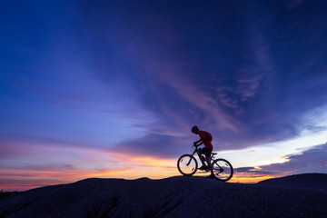 Cyclist riding mountain bike on the rocky trail at sunset.