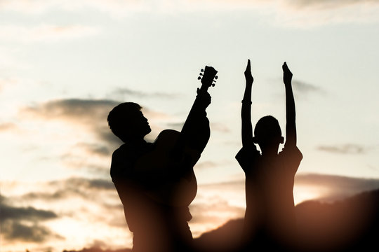 Two young christian worship God and playing guitars with light sunset background,christian silhouette concept.