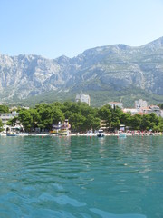 Fototapeta premium Plaża w Chorwacji w upalny letni dzień. Łódki, zjeżdżalnie i drzewa na tle gór.