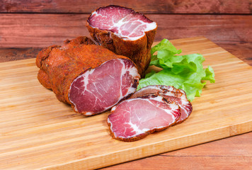 Partly sliced dried pork neck on wooden cutting board
