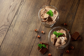 Homemade chocolate ice cream with mint leaves, sprinkled with chocolate in a glass bowl on a wooden table. chocolate pieces, hazelnuts. Selective focus, copy space.