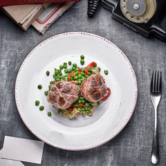 Beef medallions wrapped in bacon, serve with green peas and on a plate on wooden background. Close up