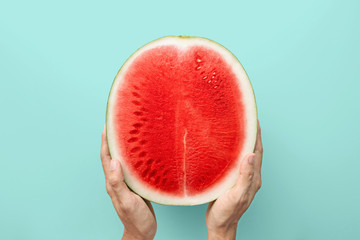 Hands holding a half of red watermelon on a blue background, top view with clipping path