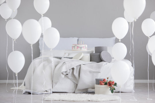 Birthday cake with candles in the middle of king size bed with grey bedding, real photo with copy space on the empty wall