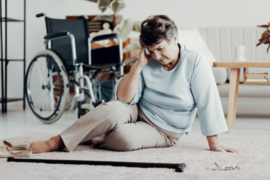 Disabled elderly woman with headache on the floor with walking stick