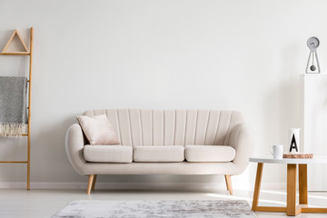 Pillow on white sofa next to wooden coffee table with mugs, copy space on empty wall
