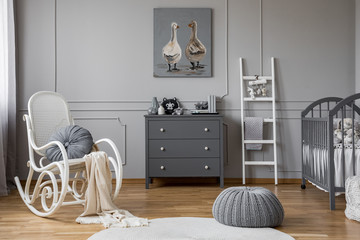 Pouf and rocking chair in grey baby's bedroom interior with ladder next to cabinet. Real photo