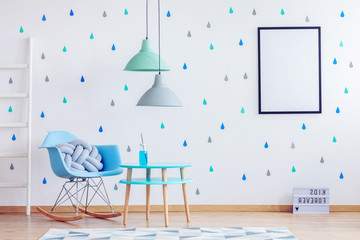 Mint green and grey lamps above blue wooden table in kid's room with white mockup poster on the wall