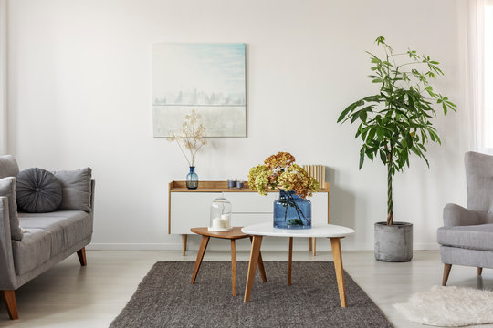 Flowers in glass blue vase on white wooden coffee table in the middle of scandinavian living room